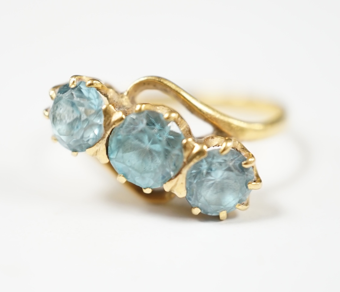 A yellow metal and three stone blue zircon set crossover ring, size L, gross weight 3 grams. Condition - poor